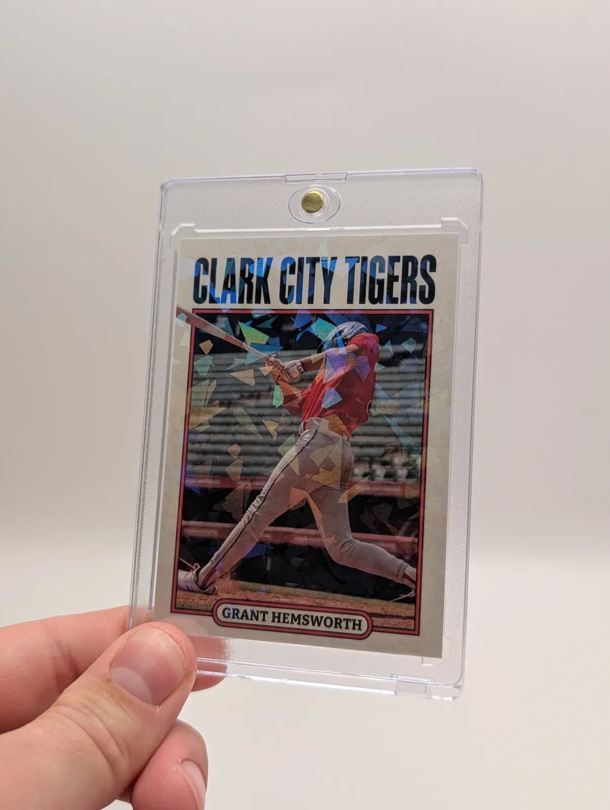 Hand holding a printed baseball card with a reflective pattern inside a clear magnetic case